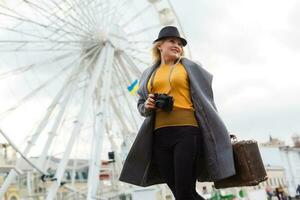 joven mujer vistiendo sombrero caminando al aire libre en el ciudad calle cerca ferris rueda sonriente alegre. foto