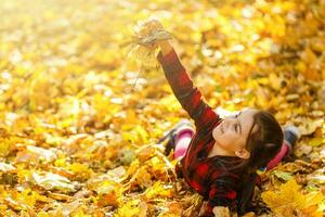 Little girl playing with fallen autumn leaves. photo