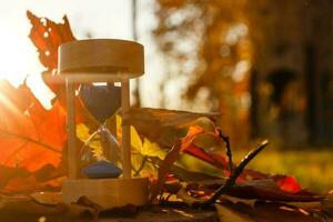 otoño hora tema, reloj de arena en caído hojas en varios colores con Copiar espacio. foto