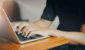 Closeup of a man's hand typing on a laptop. Typing on a laptop on a wooden table. Concept of a freelancer, writer, creative ideas photo