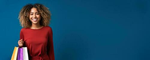 Young smiling african american woman in a red dress posing with shopping bags on a blue background black friday concept photo