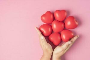 adulto manos alrededor rojo corazón en rosado antecedentes , salud cuidado, Organo donación, familia vida seguro, mundo corazón día, mundo salud día, Orando concepto foto