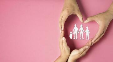 Adult hands make heart symbol around family paper on pink background. health insurance concept, healthcare,family life insurance. photo