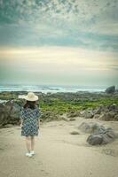 mujer con sombrero disfrutar el puesta de sol a el rocoso playa en gaia, Oporto, Portugal. foto