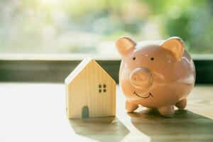 smile piggy bank with home wood house model morning sunlight background photo
