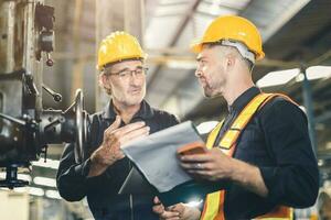 senior male worker training new young engineer employee working in heavy industry metal factory photo