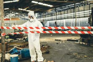 Worker in PPE safety suit with area closed barricade security tape in danger dirty area from virus infected chemical leak photo