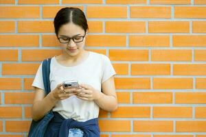 asiático adolescente niña Universidad estudiante disfrutar jugando teléfono inteligente mensaje contacto con amigos. foto
