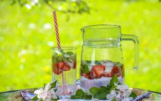 Strawberry lemonade pitcher, lemonade with lemon, lime, and strawberries, Homemade, in pitcher and glass, with many crushed ice, mint leaves, lemonade with strawberry and lemon, nature background, photo