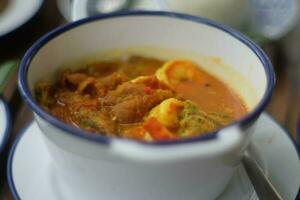 Thai style curry with fish and vegetables in a bowl on wooden table photo