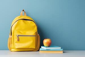 school backpack, books and apple isolated on blue background with copy space. photo
