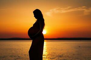 silueta de un embarazada mujer en el playa a puesta de sol. ai generado foto