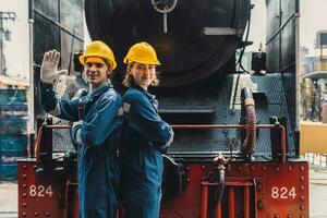 Train engineer team working service maintenance old dirty vintage classic steam engine locomotive in train repair workshop at train station. photo