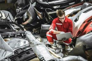 Old used car part warehouse worker checking inventory in garage. Staff worker working in recycle motor junkyard auto parts management. photo