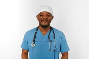 Smiling black surgeon doctor bearded man in blue coat, medical cap with stethoscope isolated white photo