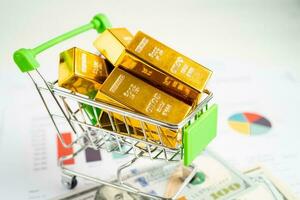 Gold bar in shopping cart on US dollar banknotes money and graph, economy finance exchange trade investment concept. photo