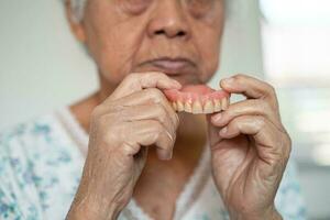 Asian elderly woman patient holding to use denture, healthy strong medical concept. photo