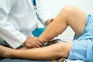 Asian doctor physiotherapist examining, massaging and treatment knee and leg of senior patient in orthopedist medical clinic nurse hospital. photo