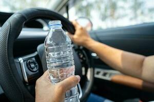 conductora asiática sosteniendo una botella para beber agua mientras conduce un automóvil. una botella de agua caliente de plástico provoca un incendio. foto
