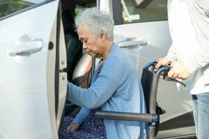 Caregiver help and support asian elderly woman sitting on wheelchair prepare get to her car to travel in holiday. photo