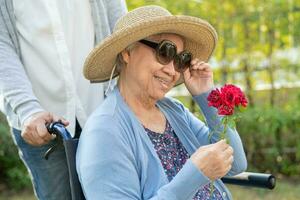 asiático mayor mujer participación rojo Rosa flor, sonrisa y contento en el soleado jardín. foto