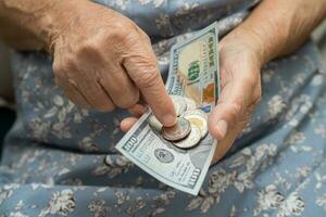 Asian senior woman holding and counting US dollar banknotes with coins money in purse. Poverty, saving problem in retirement. photo