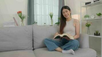 Beautiful asian young woman  reading book on sofa at home. video