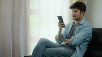 Lanza libre contento asiático hombre utilizando teléfono hablar trabajo sentado en su hogar video