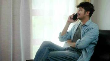 freelance gelukkig Aziatisch Mens gebruik makend van telefoon praten werk zittend in zijn huis. sucess begrip. video
