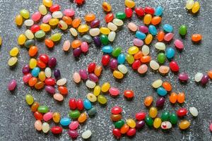 Big pile of colorful jellybeans spread out on rustic grey background photo