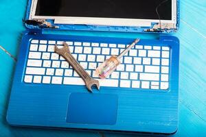 Wizard repairs laptop with tools and hands on the blue wooding table. top view. wrench and screwdriver on the keyboard photo