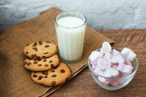 Fragrant, tasty, homemade cookies with raisins, marshmallows in the form of hearts and glass of fresh milk on the table photo