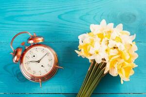 Vintage mechanical alarm clock with yellow daffodils on a blue wooden background. Good morning, we are from Ukraine photo