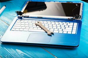 Wizard repairs laptop with tools and hands on the blue wooding table. top view. wrench and screwdriver on the keyboard photo