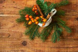 invierno, ambiente cálido. una composición con una taza con ramas de abeto y escaramujos sobre un fondo de madera foto