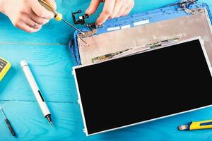 el asistente repara la computadora portátil con herramientas y manos en la mesa de madera azul. vista superior foto