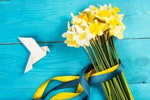 Yellow daffodils with a yellow-blue ribbon on a wooden background and a white paper's dove. Concept of Peace in Ukraine photo