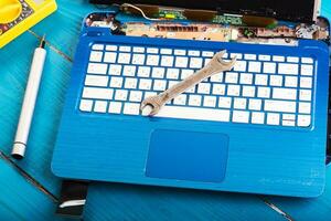 Wizard repairs laptop with tools and hands on the blue wooding table. top view. wrench and screwdriver on the keyboard photo