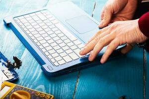 Wizard repairs laptop with tools and hands on the blue wooding table. top view photo