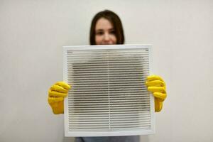 mujer sosteniendo una rejilla de ventilación sucia y polvorienta, borrosa. foto