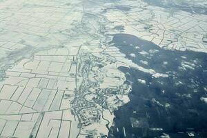Aerial cloudscape view over clouds top to snow covered rivers, roads, cities and fields, winter air photo