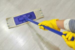 Girl in protective gloves cleaning floor using flat wet mop. photo