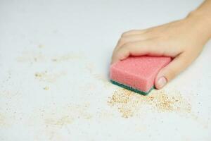 Sponge in woman hand removes dirt, bread crumbs and leftovers. Cleaning kitchen table. Household chores photo