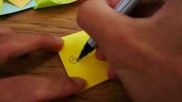 homem escrevendo boa vontade Nota em amarelo papel Nota com Preto caneta e suave foco cena. video