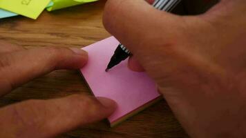 hombre escritura ingresos Nota en un rosado papel Nota con negro bolígrafo y suave atención escena. video