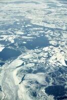 Aerial view from airplane window over clouds top to snow covered frozen sea, winter fresh frosty air photo