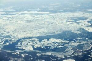 Aerial view from airplane window over clouds top to snow covered rivers, fields and roads photo