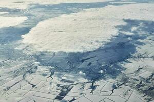 Aerial view over clouds top to snow covered rivers, fields and roads, winter fresh frosty air photo