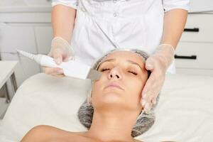 Beautician makes facial ultrasonic peeling for rejuvenation woman face skincare in beauty spa salon photo