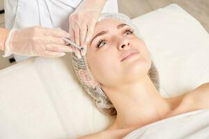 cosmetólogo hace inyección de rejuvenecimiento en la cara de la mujer, procedimiento antienvejecimiento en salón de belleza foto